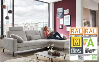 Großes graues Ecksofa im modernen Wohnzimmer mit RAL Gütezeichen Möbelqualität. Die Frau liest entspannt auf dem Sofa, das mit Kissen und Couchtisch mit Deko ausgestattet ist.